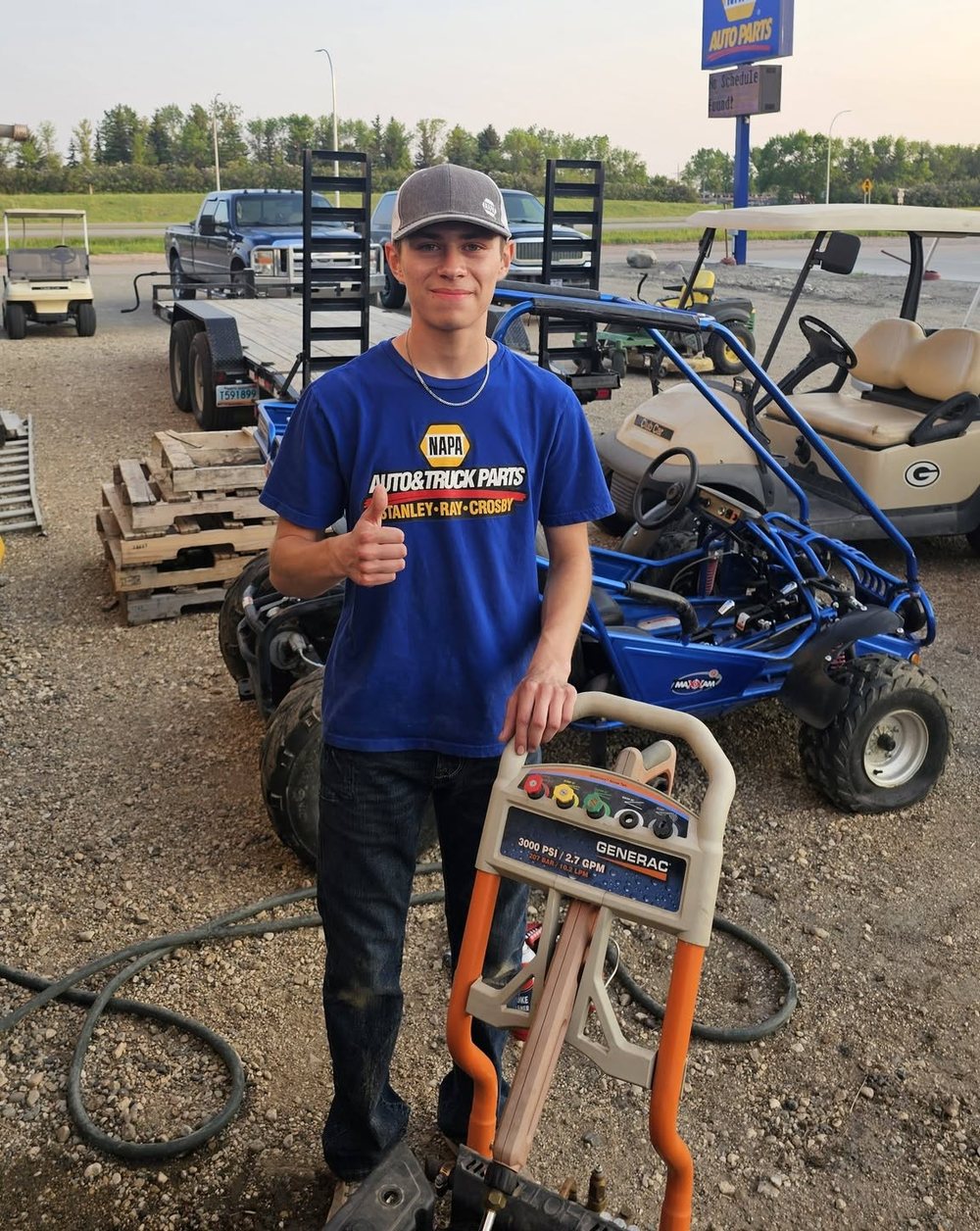 Oscar Garcia, Whips Garage maintenance tech, giving a thumbs up next to a pressure washer and a go-kart
