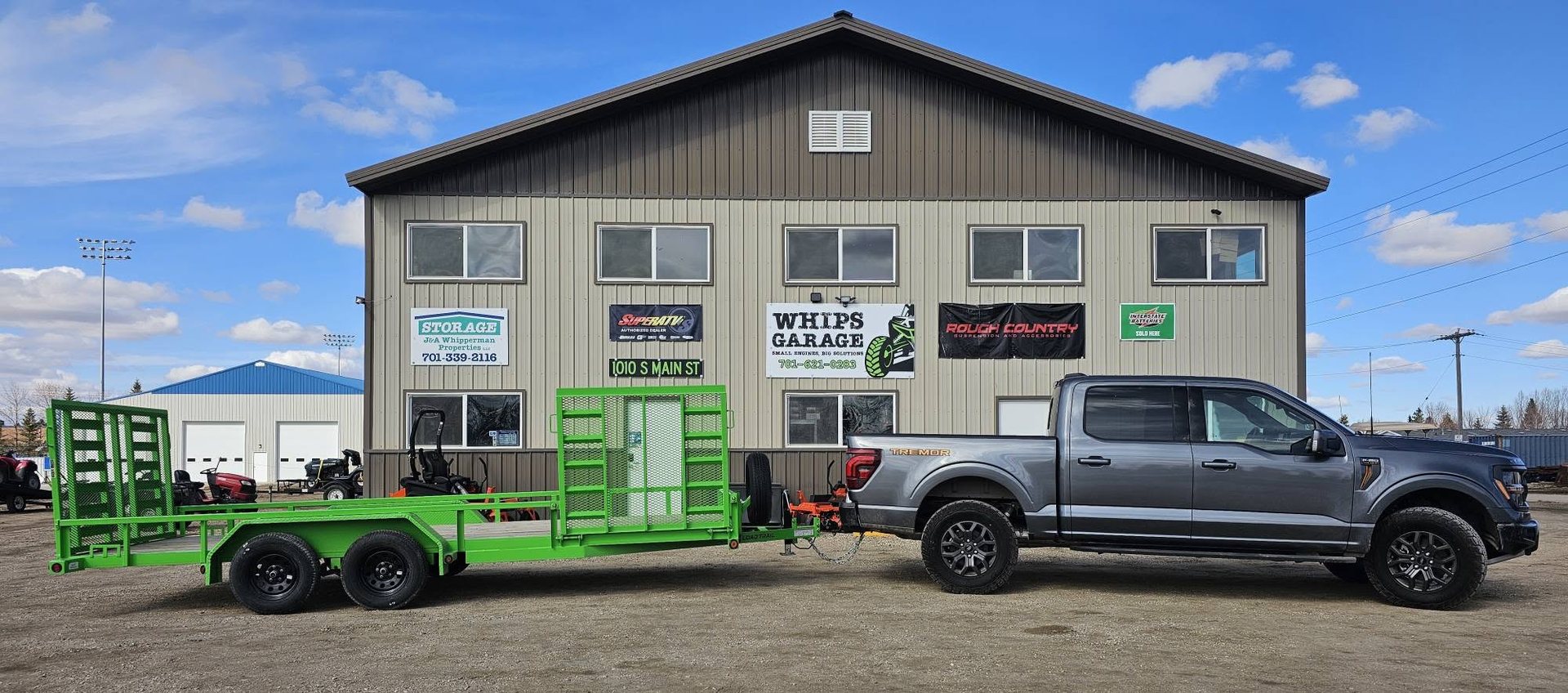 The Whips Garage shop at 1010 S Main St in Stanley, with a green trailer and pickup parked out front
