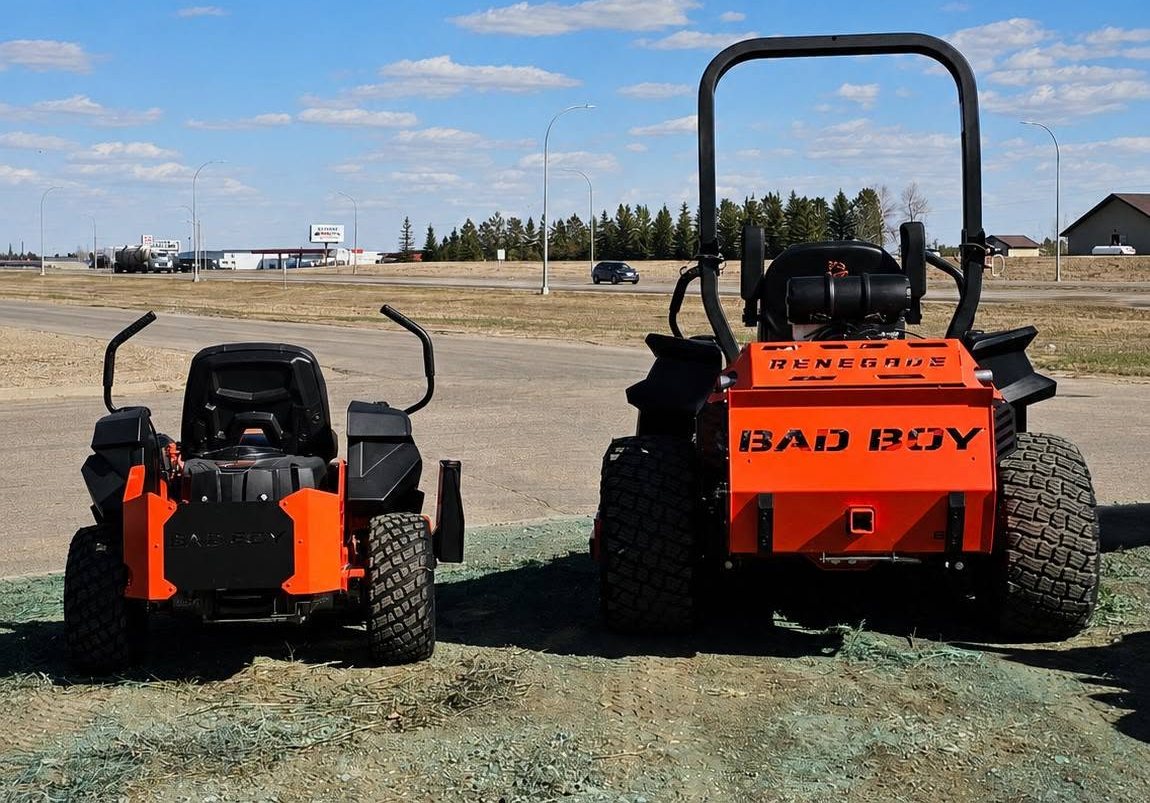 Two orange Bad Boy zero-turn mowers, including a Renegade, parked outside